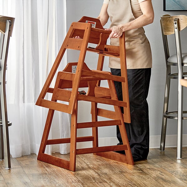 A woman holding an unassembled Lancaster Table & Seating wooden high chair.