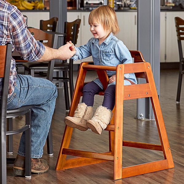 A man holding a child's hand as she sits in a Lancaster Table & Seating wooden high chair.