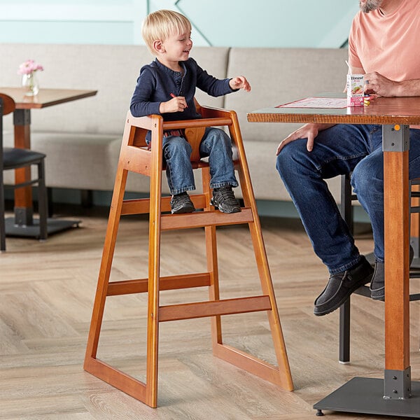 A man sitting at a table with a child in a Lancaster Table & Seating wooden high chair.