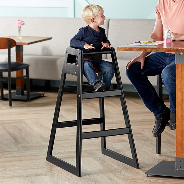 A young boy sitting in a Lancaster Table & Seating black wooden high chair.