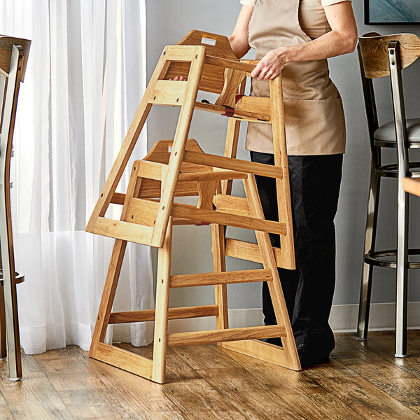 A woman standing next to a Lancaster Table & Seating wooden high chair with a natural finish.