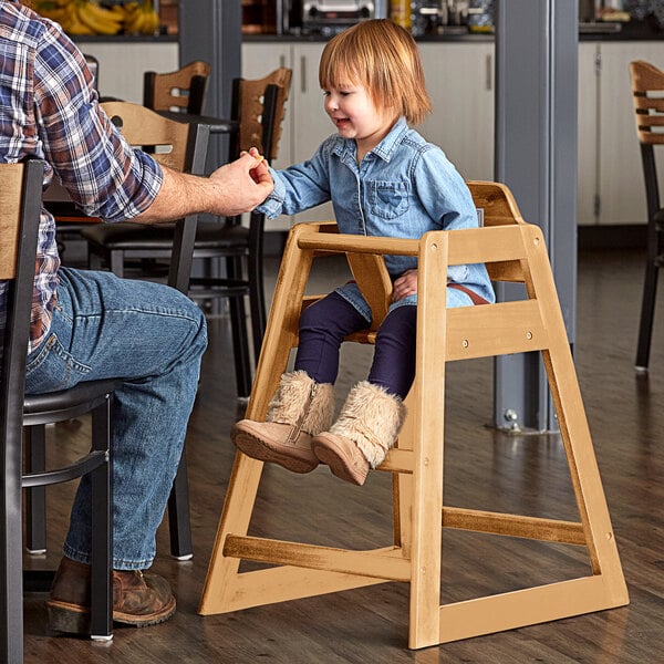 A man sitting at a table with a child sitting in a Lancaster Table & Seating wooden high chair.