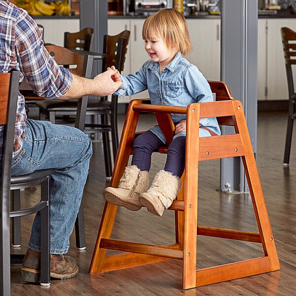 A man helping a little girl sit in a Lancaster Table & Seating wooden high chair.