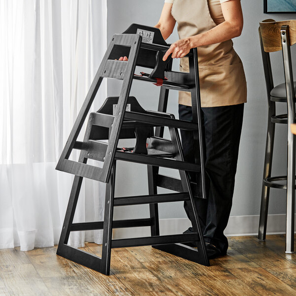 A person holding an unassembled black wooden high chair.