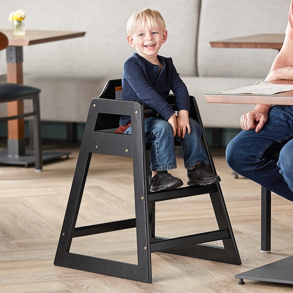 A child sitting in a Lancaster Table & Seating high chair with a black finish.