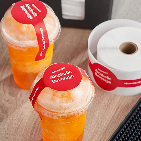 Two plastic cups of orange liquid with TamperSafe red paper drink labels on top.