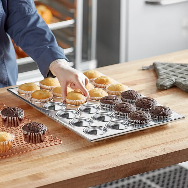 A person picking up a tray of cupcakes from a Thunder Group aluminum muffin pan.