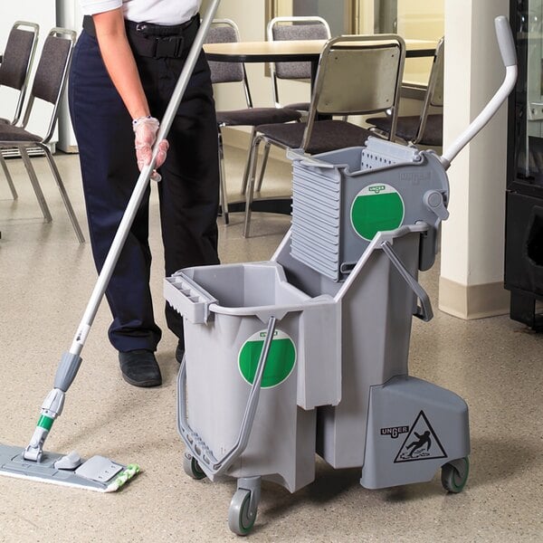 A woman mopping the floor in a room with a Unger grey mop bucket.