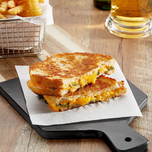 A grilled Armored Fresh vegan American cheese sandwich cut in half on a cutting board next to a glass of beer and fries.