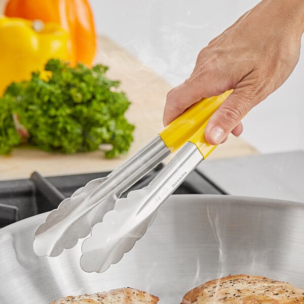 A hand using Fourt&#233; scalloped tongs with a yellow handle to cook food.