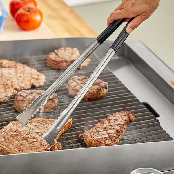 A person using Fourté stainless steel grill tongs to cook meat on a grill.