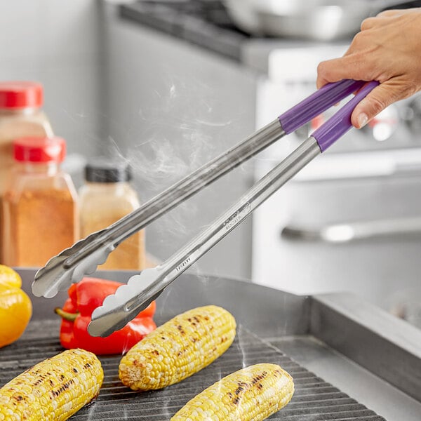 A person using Fourt&#233; purple stainless steel scalloped tongs to cook corn on the cob.