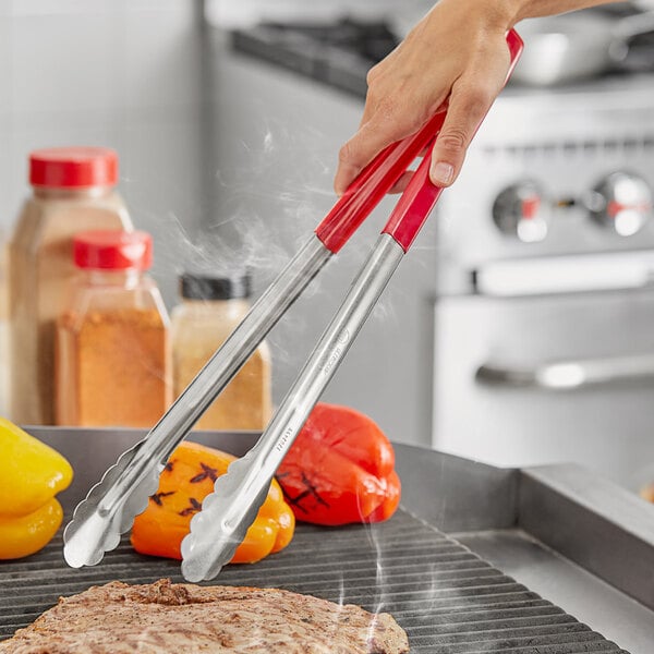 A person using Fourt&#233; stainless steel scalloped tongs with red coated handles to grill food.