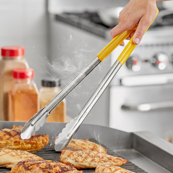 A person using Fourté yellow stainless steel scalloped tongs to grill food.