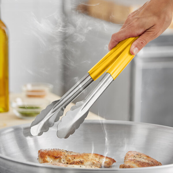 A hand using Fourté yellow stainless steel scalloped tongs to serve food.