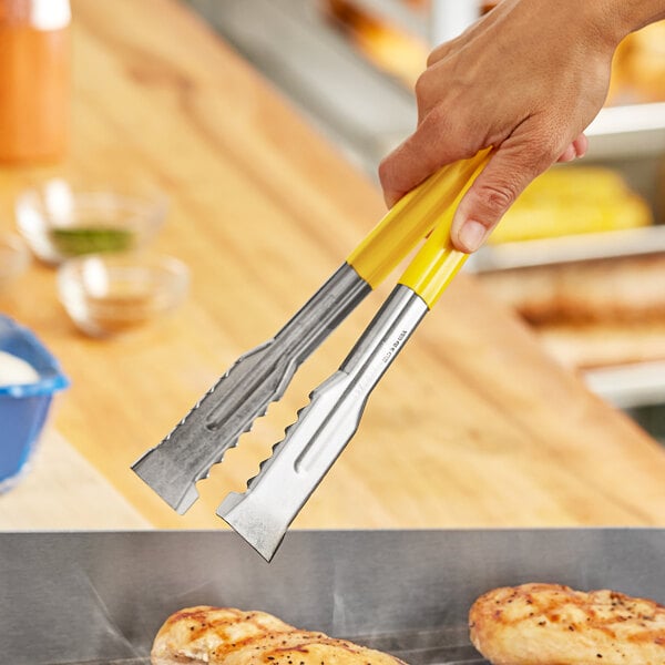 A hand holding Fourté stainless steel grill tongs with yellow coated handles