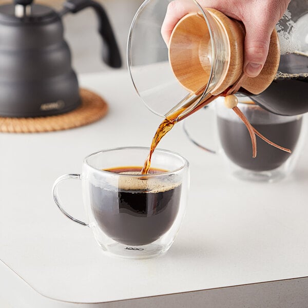 A person pouring Arrosto Kenya AA whole bean coffee into a glass cup.