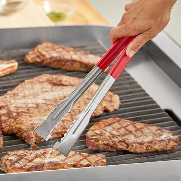 A person using Fourt&#233; red stainless steel tongs to cook meat on a grill.