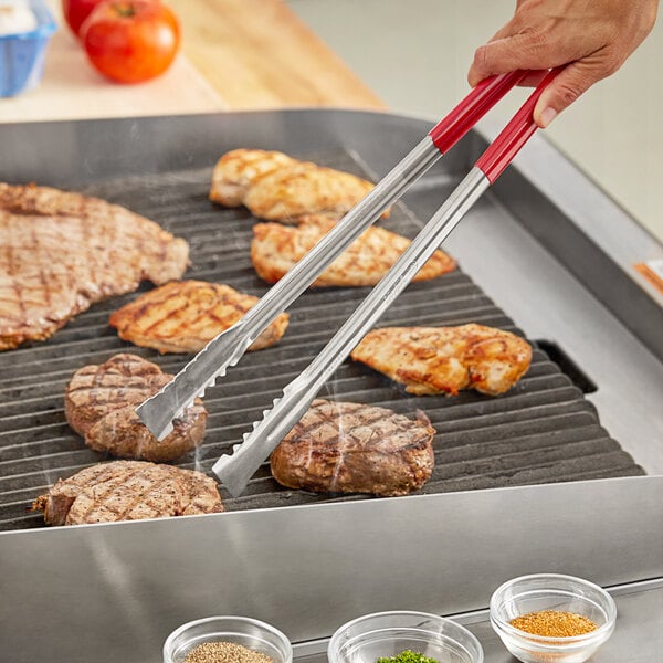 A person using Fourt&#233; red stainless steel tongs to grill meat.