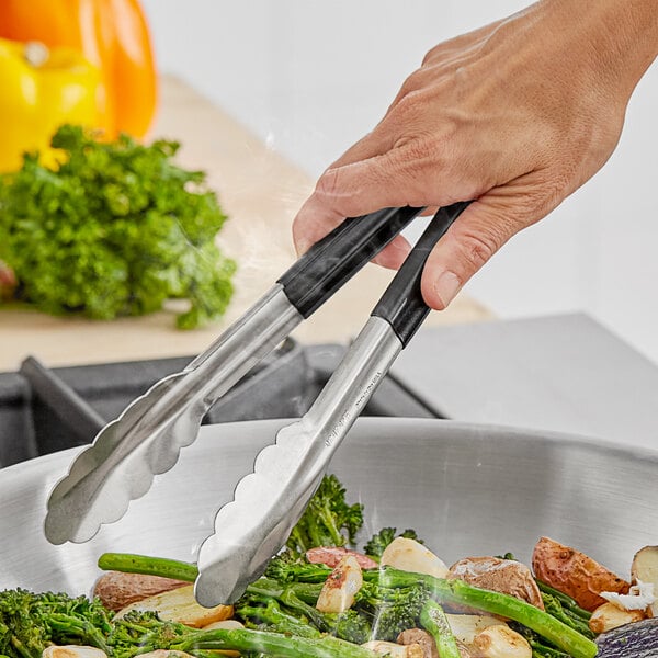 A person using Fourt&#233; black stainless steel tongs to serve green vegetables.