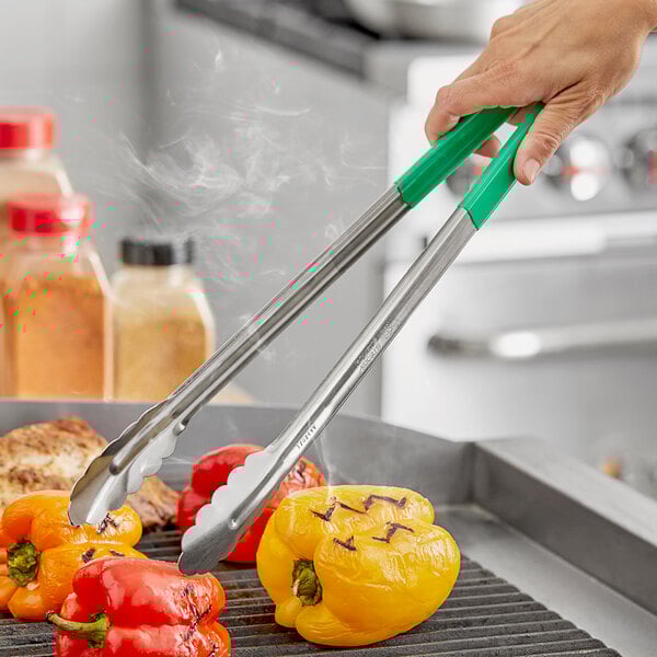 A person using Fourté green stainless steel scalloped tongs to cook peppers on a grill.