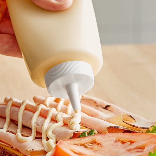 A hand using a Choice squeeze bottle lid to pour mayonnaise on a sandwich.