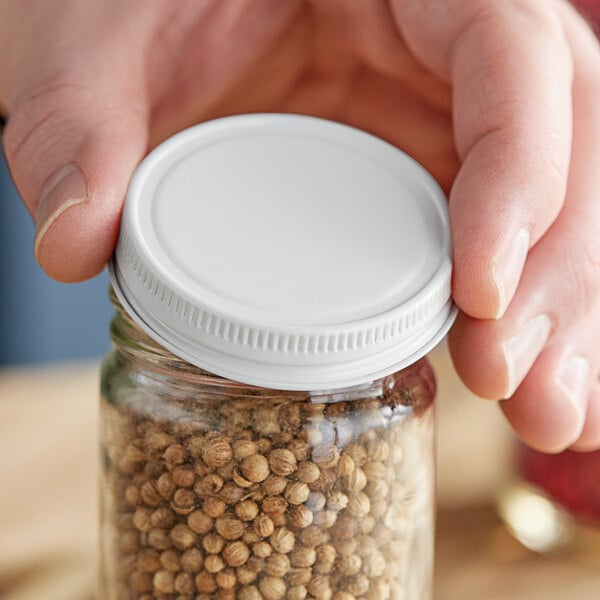 A hand holding a jar with a white metal lid containing spices.