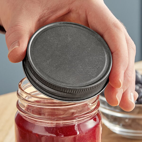 A person's hand holding a 70/450 Pewter Gray metal lid on a jar.