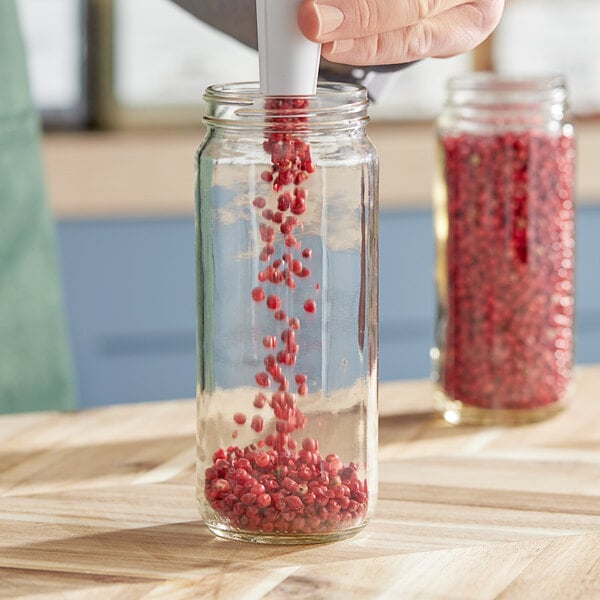 A person's hand pouring red pepper into a Paragon glass jar.