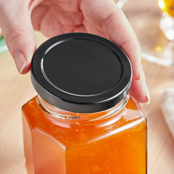 A person holding a jar with a 63 Lug black metal lid on it.