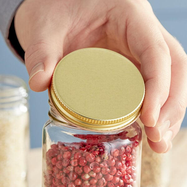 A hand holding a jar of red pepper with a gold metal lid.