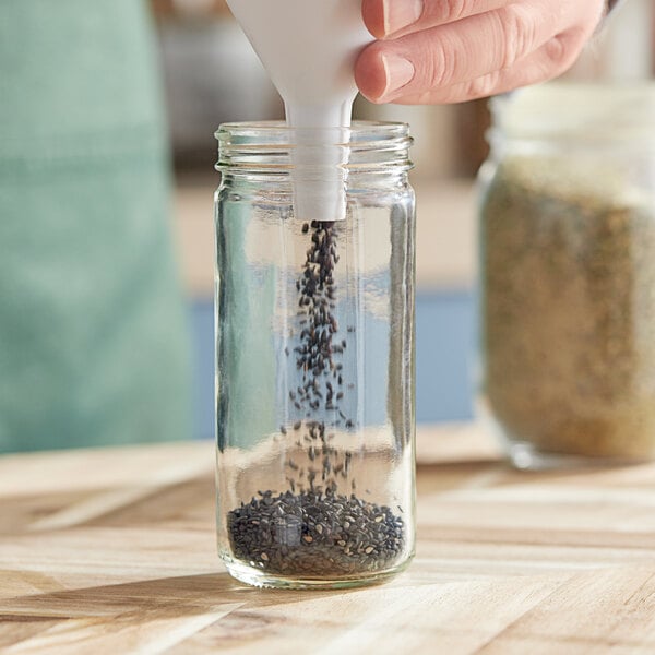 A person pouring black seeds from a glass jar.