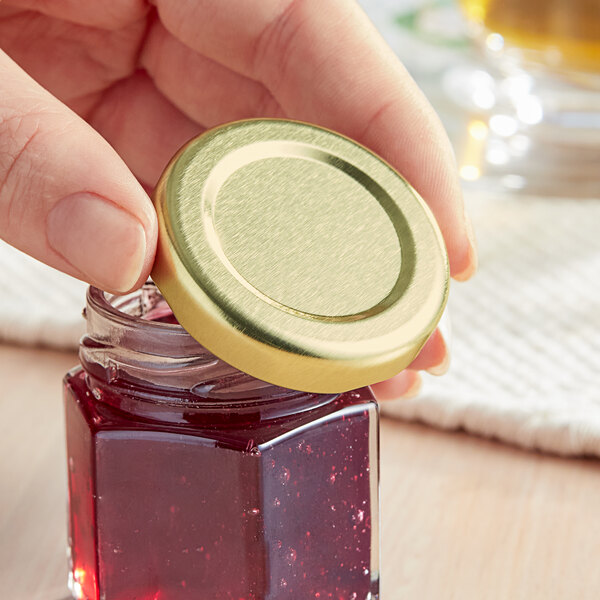 A hand holding a jar with a gold metal lid.