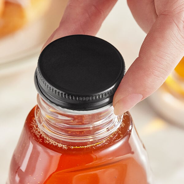 A hand holding a small bottle of liquid with a black metal lid.