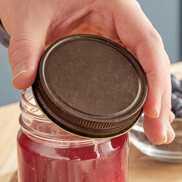 A person holding a jar of jam with a Rustic Brown metal lid.