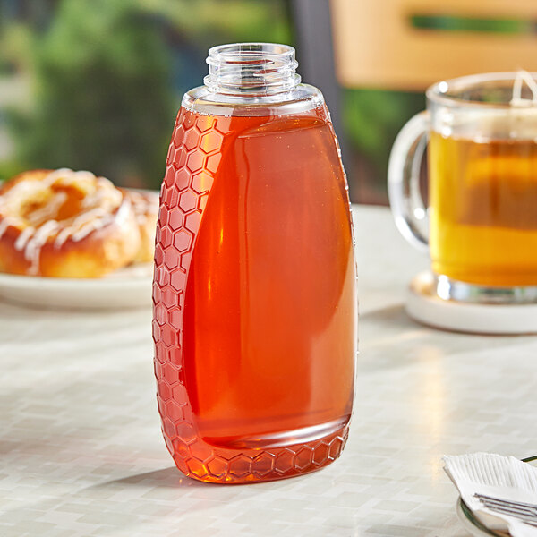 A 16 oz. honeycomb PET inverted honey bottle on a table with a plate of honey.