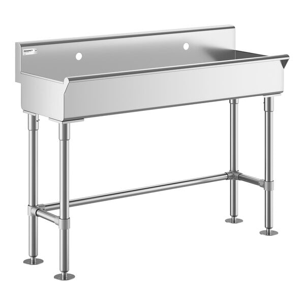 A stainless steel utility sink with four legs, a high backsplash, and two faucet holes.