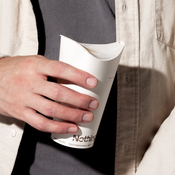 A person holding a white 8 oz. all-in-one paper hot cup with an integrated lid.