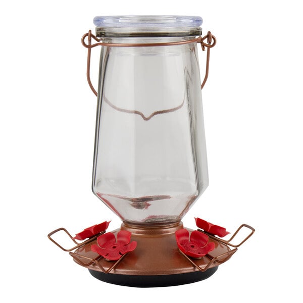 A glass jar with a metal base and red flowers on the top.