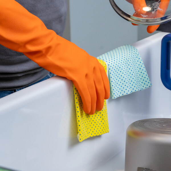 A pair of orange latex rubber gloves being used for cleaning in a kitchen setting.