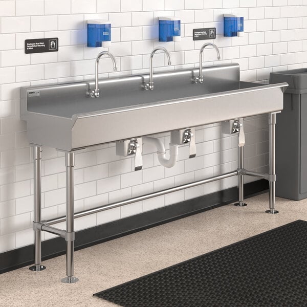 A Regency stainless steel hand sink with 3 knee-operated faucets over a counter.