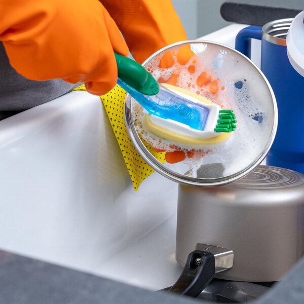 A pair of orange latex rubber gloves being used to wash dishes in a sink.