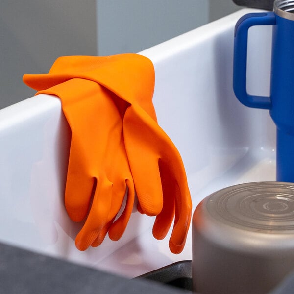A pair of orange latex rubber gloves draped over the edge of a white sink.