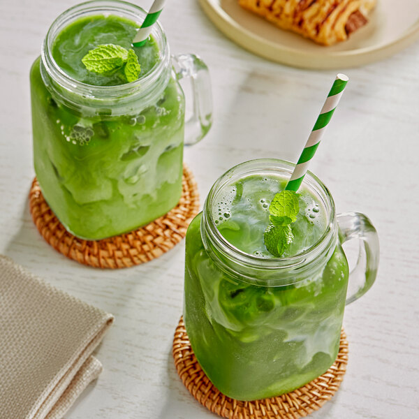 Two mason jars of green Matcha lattes with straws on a table.