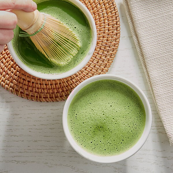 A hand holding a whisk in a bowl of green tea.
