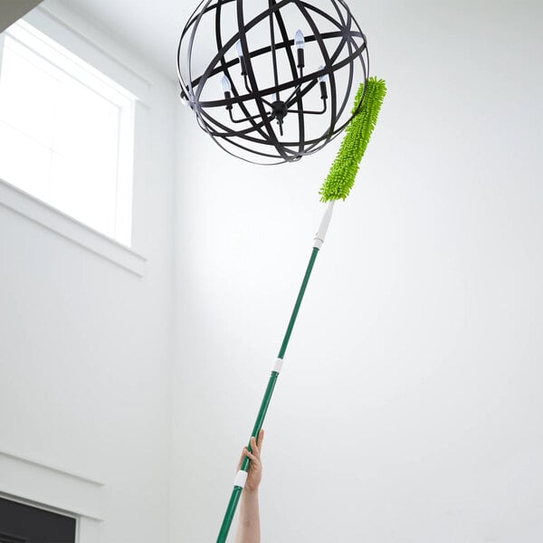 A green flexible microfiber wand duster with an extendable handle being used to clean a high light fixture.