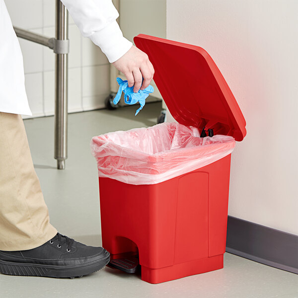 A hand putting a blue glove into a red Lavex step-on trash can.