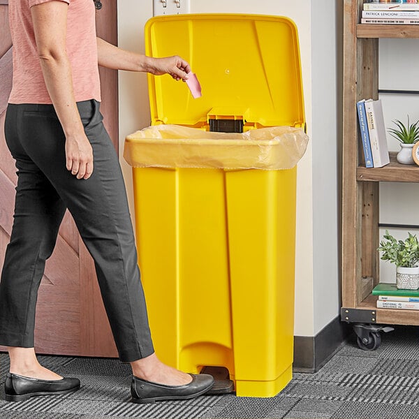 A woman standing next to a Lavex yellow rectangular step-on trash can.