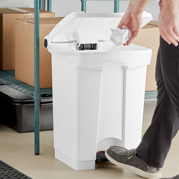 A person using a Lavex white rectangular step-on trash can.