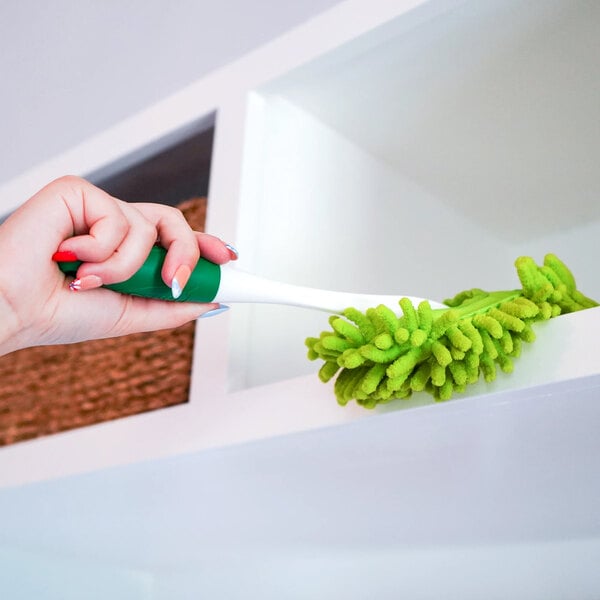 A green and white microfiber duster being used to clean a shelf.